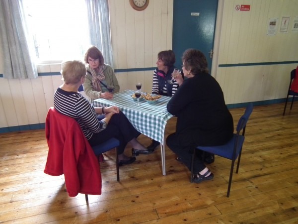 Four women chatting around a table inside the village hall at book launch